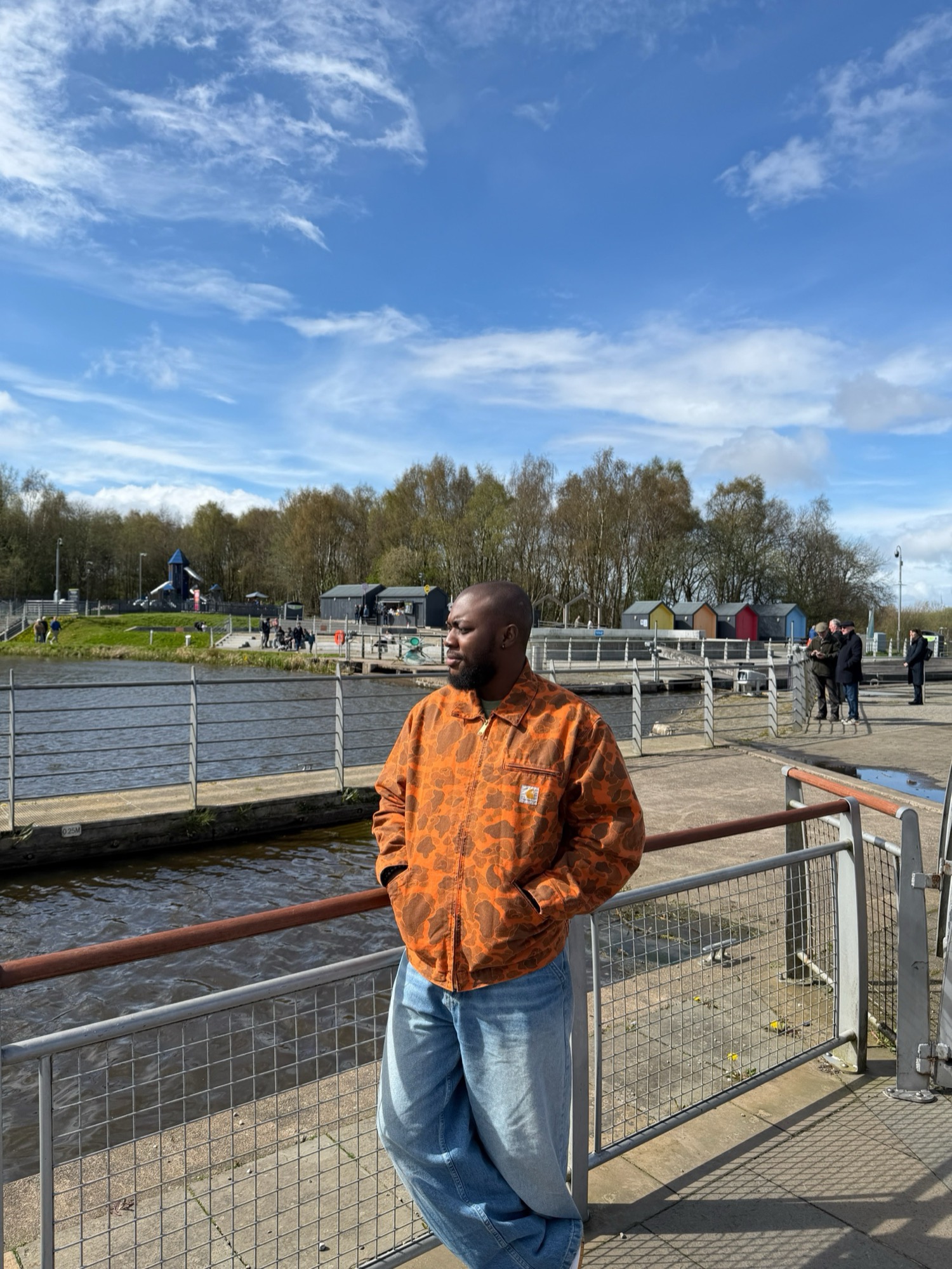 Emmanuel Oshowobi standing by a canal, hands in pockets, in an orange jacket.